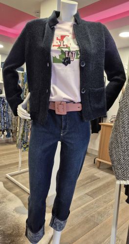 Tenue féminine tendance avec jean bleu, cardigan noir, tee-shirt imprimé et ceinture rose.